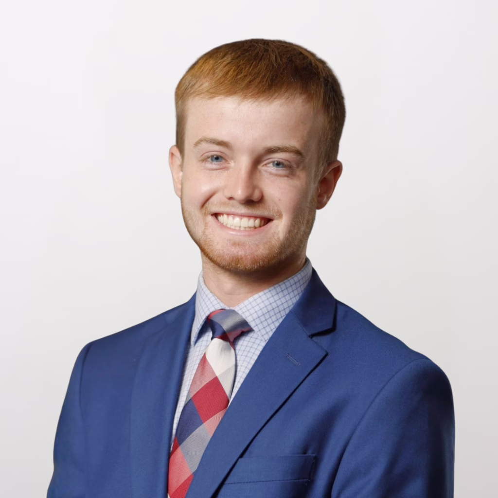 Smiling man in a blue suit and plaid tie, posing for a professional headshot against a light background.